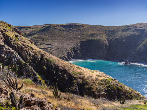 Desert landscape with rugged cliffs overlooking a tranquil bay with clear blue water.   Mirador Punta Lobas, Baja California Sur, Mexico