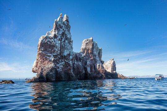 Majestic rock formations rise above the calm ocean under a clear blue sky. Canada