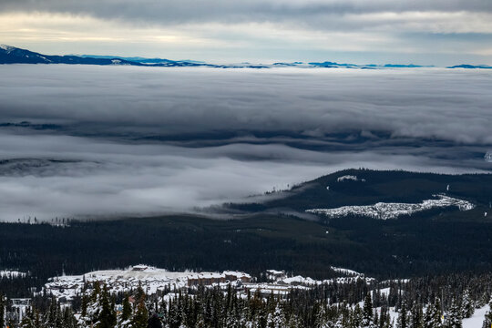 Cloudy sky over snow-capped mountains with dense forest and distant horizon.   Kootenay Boundary, British Columbia, Canada