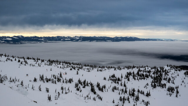Snow-covered mountain landscape with cloudy skies and distant mountain range at sunrise. Kootenay Boundary, British Columbia, Canada