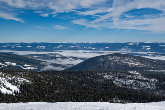 Snow-covered mountainous landscape with dense forests under a clear blue sky. Kootenay Boundary, British Columbia, Canada