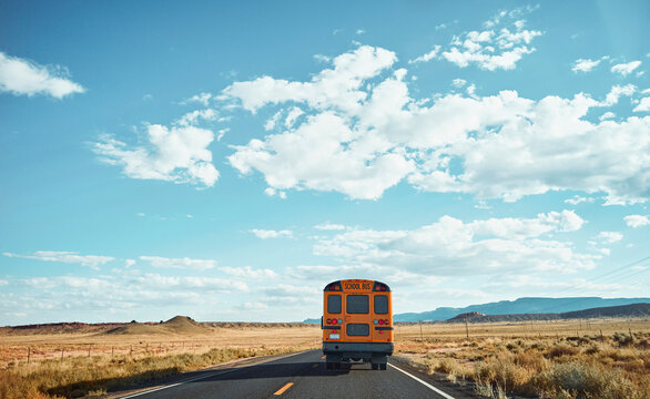 Yellow school bus driving through vast desert landscape under a blue sky with clouds. Monument Valley, Arizona, USA
