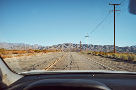 View through a car windshield of an empty desert road with mountains and power lines. California, USA