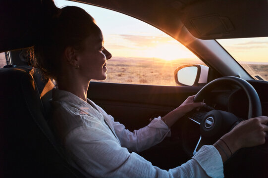 Woman driving a car at sunset through a scenic rural landscape. California, USA