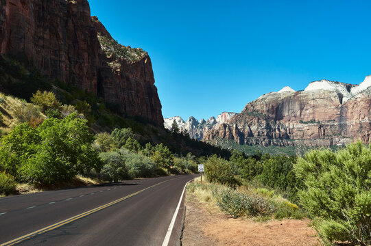 Scenic road flanked by towering mountains under a clear blue sky in a desert landscape. Zion National Park, Utah, USA