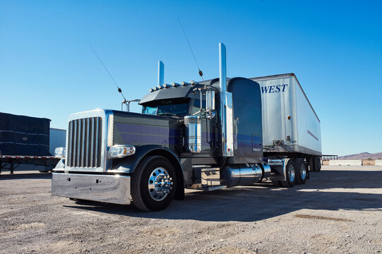 A shiny blue and chrome semi-truck parked in a sunny, open parking lot with clear blue sky. Arizona, USA