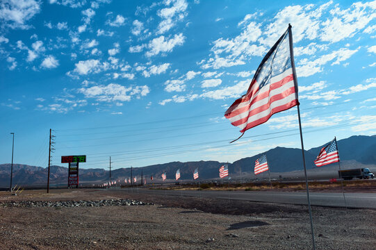 American flags fluttering near a highway with mountains and a partly cloudy sky. Arizona, USA