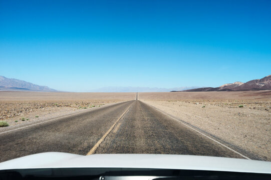 Straight desert road leads to distant mountains under a clear blue sky. Death Valley, California, USA