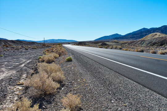Desert highway stretching into distant mountains under a clear blue sky. Death Valley, California, USA