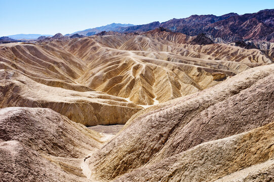 Vast desert landscape with layered sandstone and mountains under a clear blue sky. Death Valley, California, USA