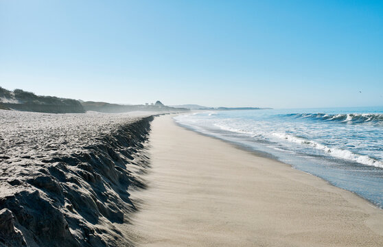 Sandy beach with gentle waves under a clear blue sky and distant coastline. Half Moon Bay, California, USA