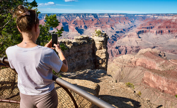A woman takes a photo with her phone at the edge of the Grand Canyon with stunning views. Grand Canyon, Arizona, USA