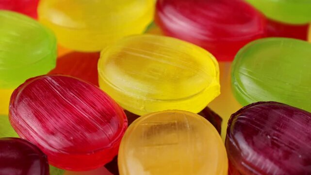 Glossy fruit-flavored hard candies in red, yellow, and green colors circle rotation close up