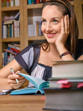 Smiling woman reading a book at a desk piled with books in a cozy library setting Germany