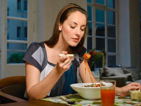 Woman enjoying a bowl of spaghetti at a dining table indoors. Germany