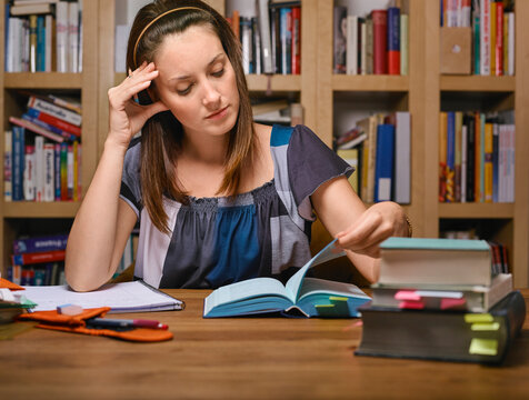Woman reading books at a table in a library with shelves in the background. Germany