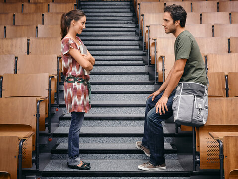 Two young adults conversing on empty lecture hall steps with wooden seats. Germany