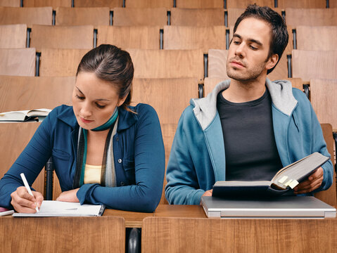 Two young adults in a lecture hall, one taking notes and the other reading a book.   Germany