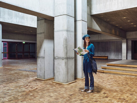 Woman in a hat reading map in a modern, concrete architectural space. Germany