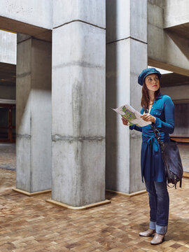 Woman in casual attire holding a map stands in a modern concrete building. Germany