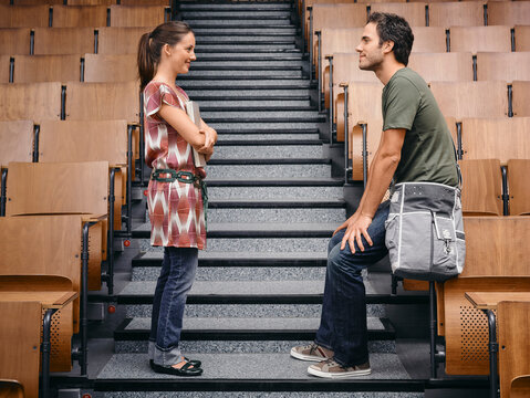 Two young adults in casual attire chat on stairs in an empty lecture hall. Germany