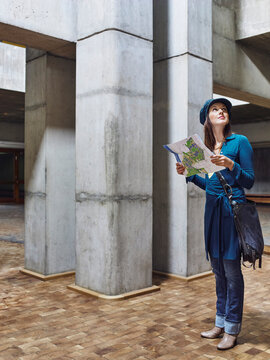 Woman in blue holding a map, standing in a concrete architectural space. Germany