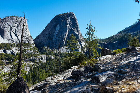 Rocky mountain landscape with trees, clear blue sky, and rugged terrain under sunlight. Yosemite National Park, California, USA