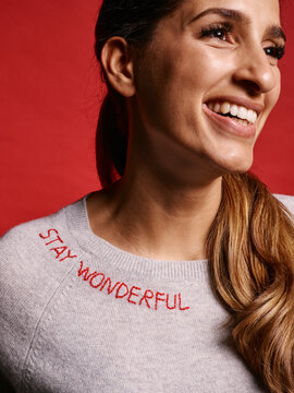 Smiling woman with long hair in a sweater that says Stay Wonderful on red background. Germany