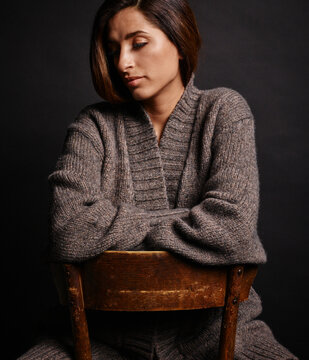 Woman in a cozy knitted sweater sitting on a wooden chair with a dark background Germany