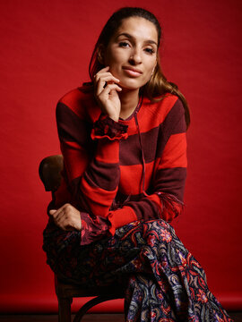 Woman in red striped sweater sitting on a chair with a red backdrop. Germany