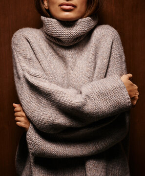 Woman in a cozy oversized turtleneck sweater hugging herself against a wooden backdrop. Germany