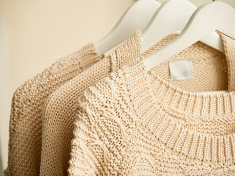 Cream-colored knitted sweaters on white hangers against a beige backdrop. Germany