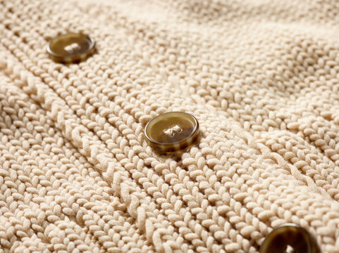 Close-up of beige knitted fabric with brown buttons arranged in a vertical line. Germany