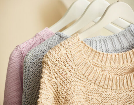 Three knitted sweaters in pastel colors hang on white hangers. Germany