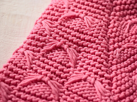 Close-up of pink knitted fabric with textured patterns on a light background.   Germany