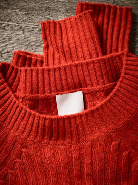 Close-up of folded red knit sweaters with ribbed collars on wooden surface. Germany