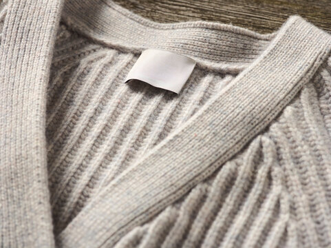 Close-up of a beige knitted sweater with a blank label on wooden background. Germany