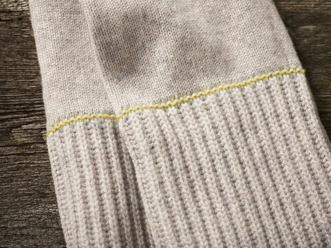 Close-up of a gray knit sleeve with yellow stitching on a wooden surface. Germany