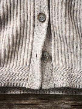 Close-up of a beige ribbed knitted cardigan with wooden buttons on wooden background Germany