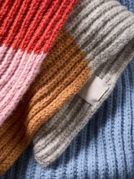 Colorful knitted scarves stacked with red, pink, orange, gray, and blue fabric textures. Germany
