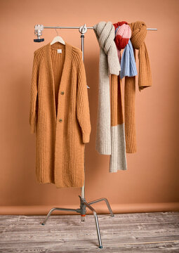 Cozy knitted cardigan and scarves on a metal rack with a warm brown background. Germany