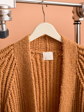 Brown knitted cardigan on a white hanger against a peach background. Germany
