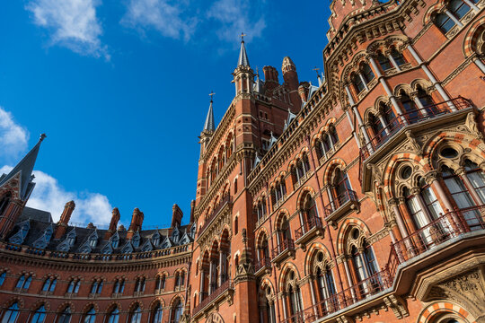 Historical red brick building with ornate arches and spires under a bright blue sky. London, UK
