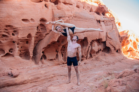 A man lifts a woman in a dramatic pose against a red rock canyon backdrop. WA, USA