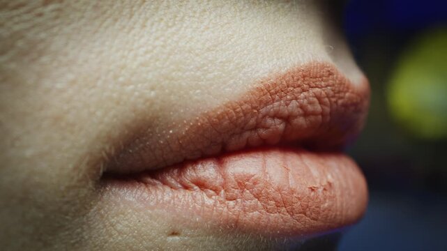 Side profile macro view of female lips wearing peach matte lipstick, showing detailed skin pores and lip texture