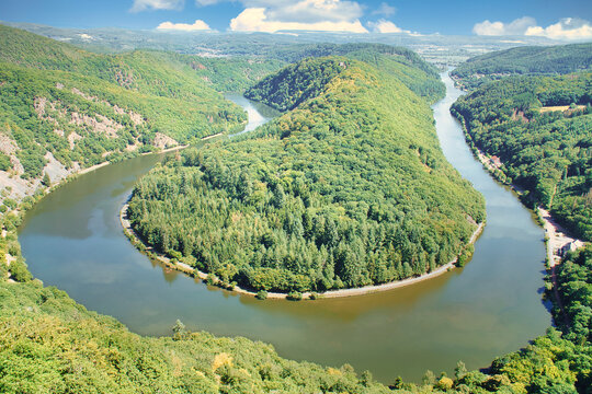 Panorama of the Saar Loop near Orscholz. The river winds in a striking curve through the dense, green forest under a blue summer sky. Top view.