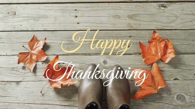 Resting leather boots on plank surface flanking orange red leaves displaying Happy Thanksgiving