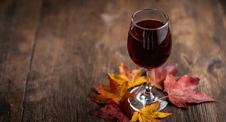 Naklejka premium Photo capturing a red wine glass and autumn colored leaves on a blurred rustic wood texture with copy space