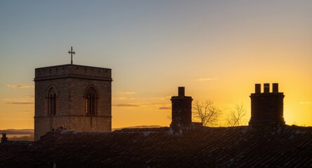 Obraz premium Rustic church tower and chimney tops set before a golden hour sky