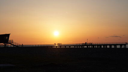 Obraz premium Silhouetted figures on pier at sunset with lifeguard tower in background